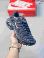 Angled front-side view of a black Nike Air Max Plus TN sneaker showing the textured upper, layered side panels, and sculpted sole.