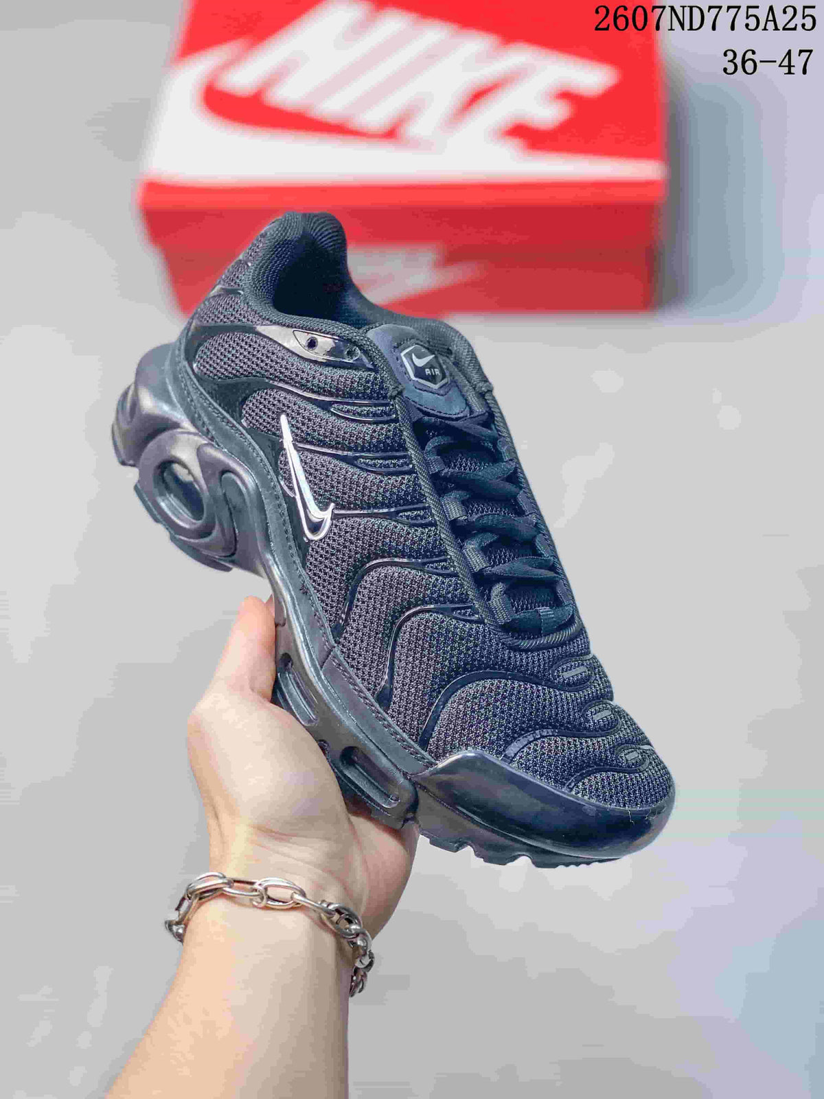 Angled front-side view of a black Nike Air Max Plus TN sneaker showing the textured upper, layered side panels, and sculpted sole.