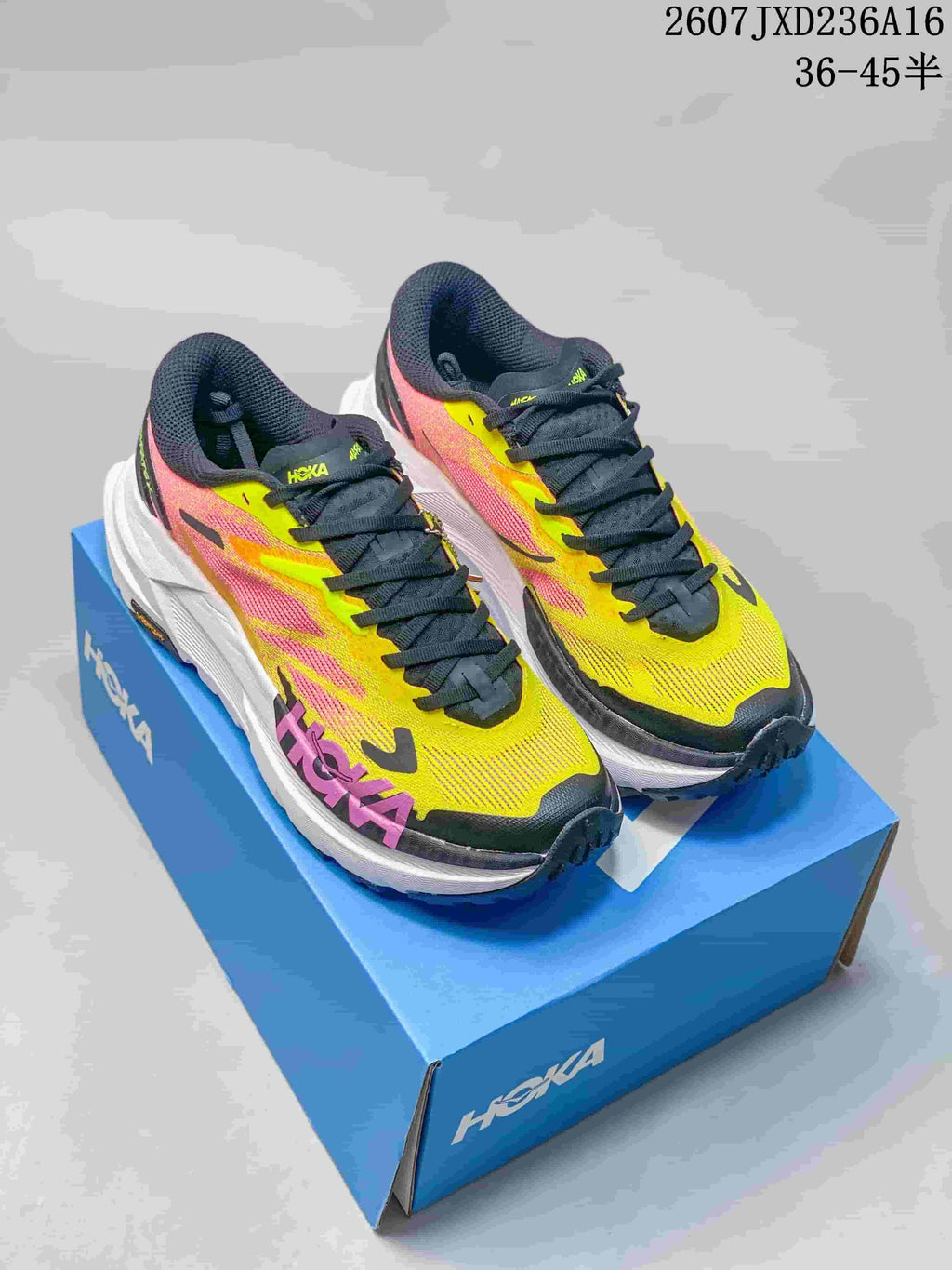 Pair of yellow, pink, black, and white Hoka MAFATE X trail running shoes displayed on a blue shoebox.