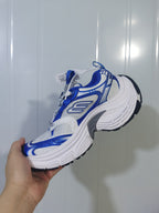 Side view of the white and royal blue sneaker showing layered upper panels, a raised white midsole, and black outsole sections.