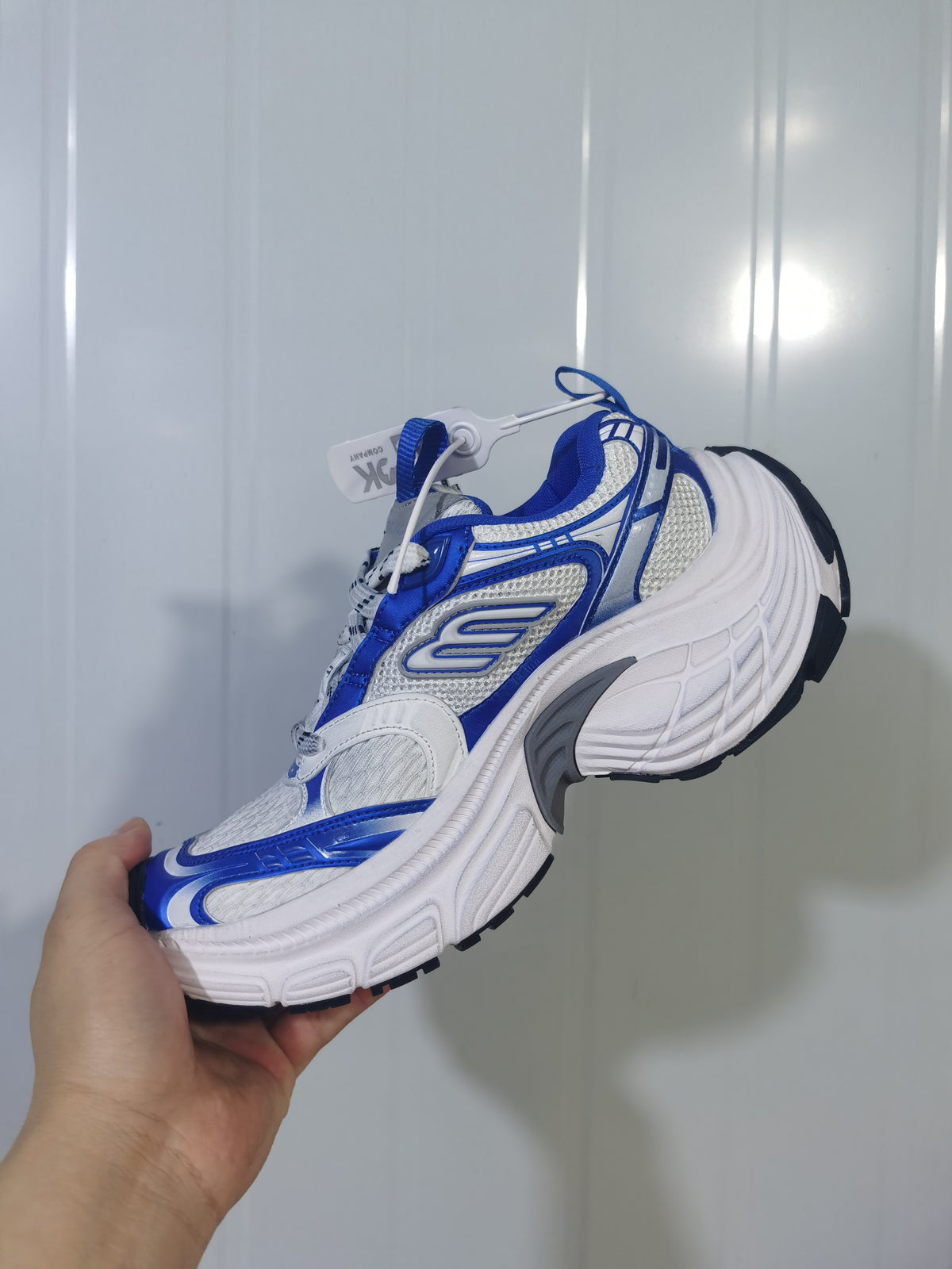 Side view of the white and royal blue sneaker showing layered upper panels, a raised white midsole, and black outsole sections.