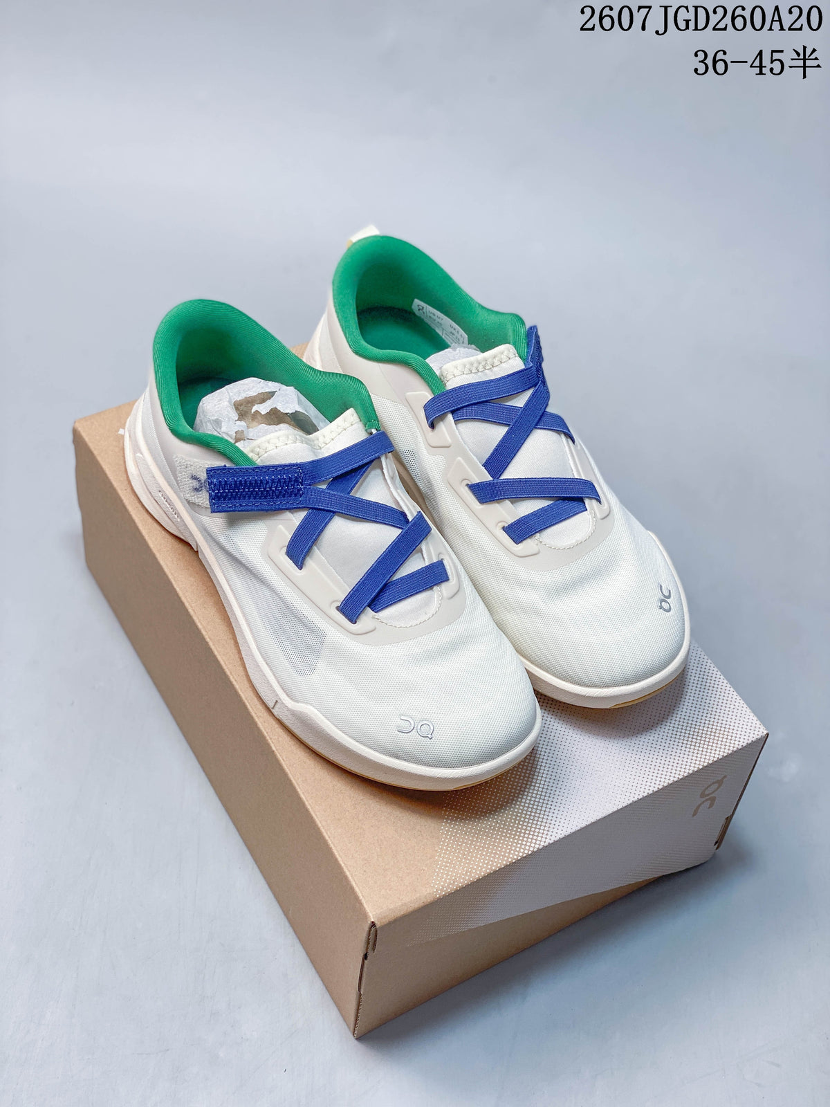 Pair of white On Cloudnova sneakers with blue crossing straps and green collars displayed on a shoebox; style code and size range are overlaid above.