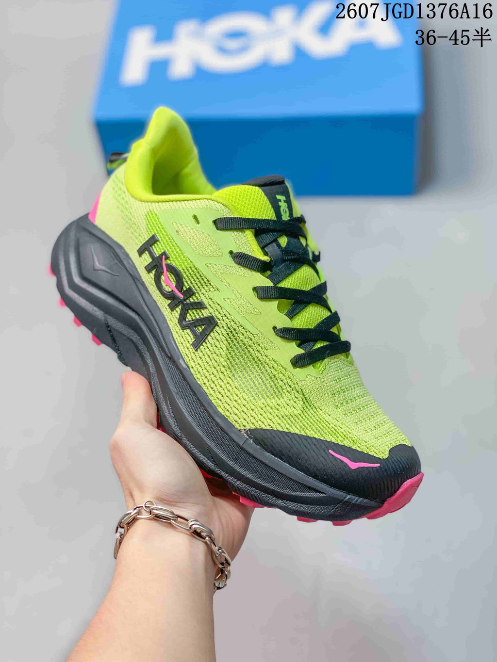 Angled side view of the HOKA running shoe showing the green upper, black midsole, and pink outsole.