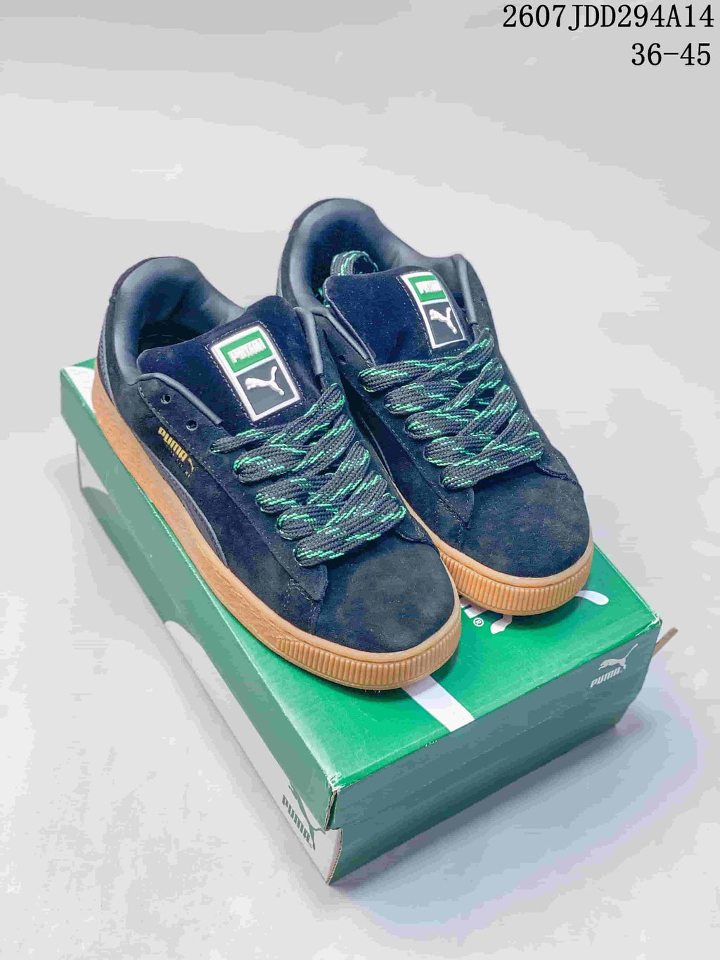 Pair of dark PUMA Suede XL low-top sneakers with green-accented laces and gum soles displayed on a green shoebox.