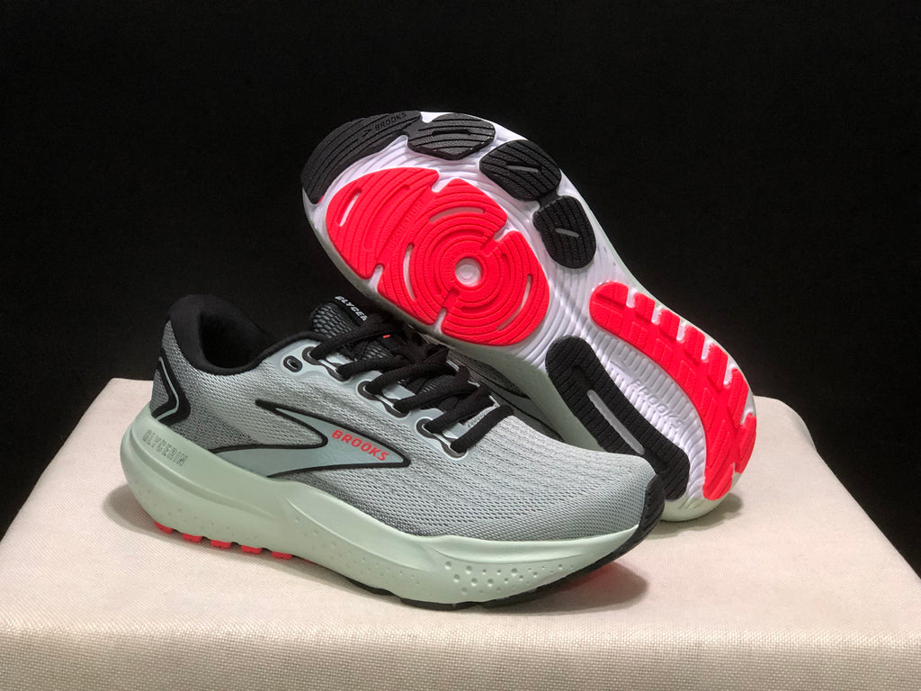 Angled view showing one sneaker's outsole with black and red traction sections and the sculpted midsole.