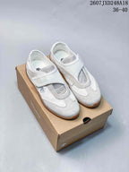 Pair of white low-top sneakers with wide straps and layered panel detailing displayed on a shoebox.