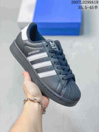 Black adidas Superstar sneaker with white serrated stripes, white heel detail, and a dark textured shell toe.