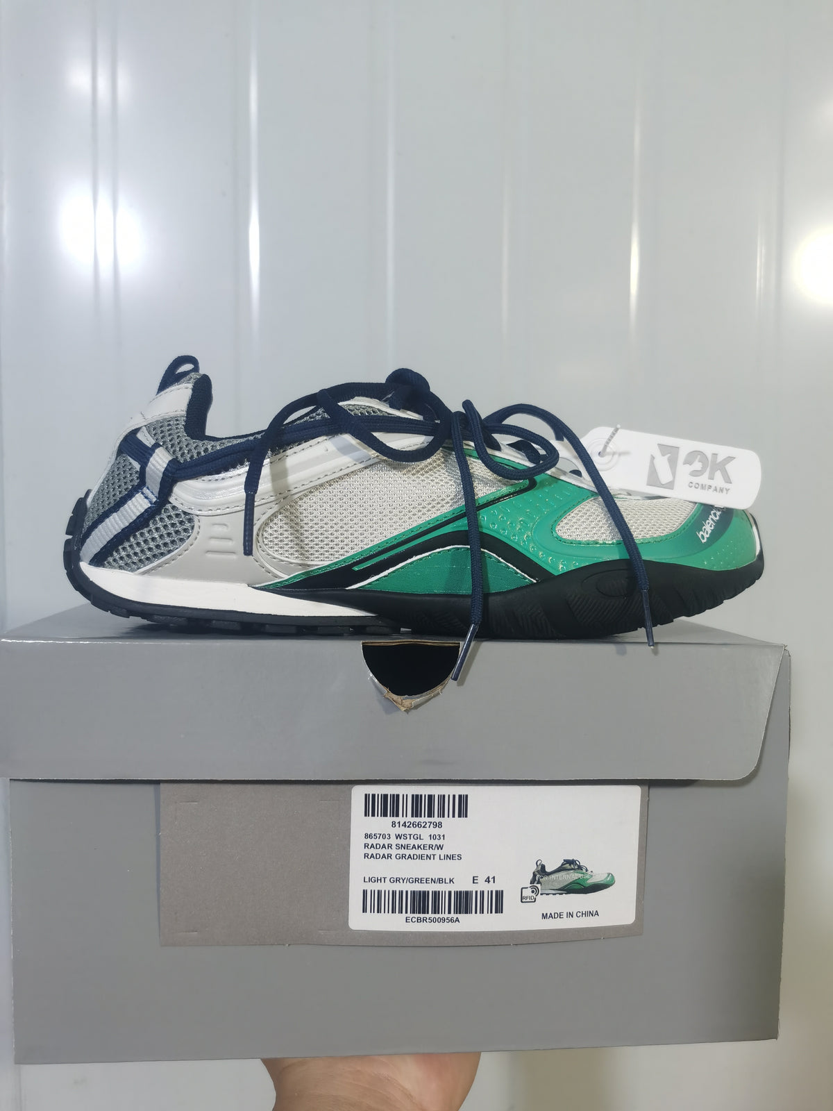 Side view of a Balenciaga Radar sneaker in light grey, green and black, displayed on its shoebox with the product label visible.