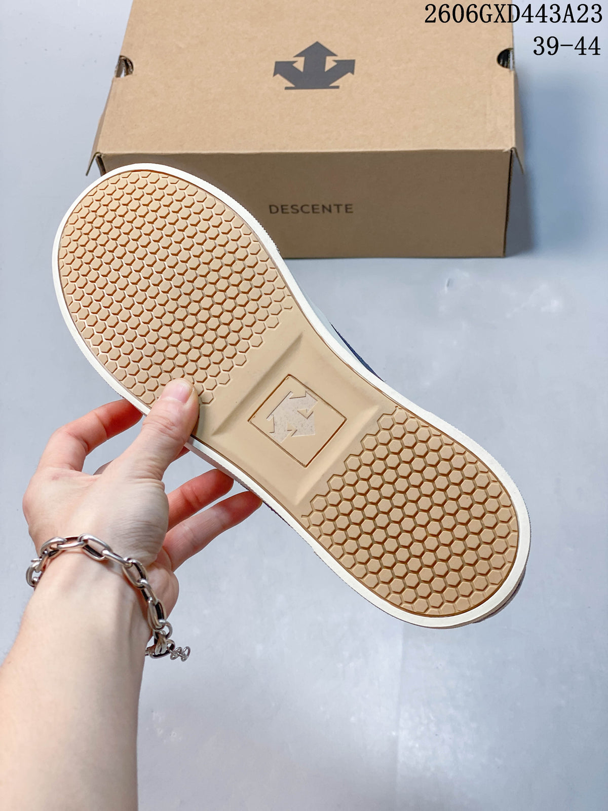 Honeycomb-patterned outsole of the blue DESCENTE sneaker beside its box