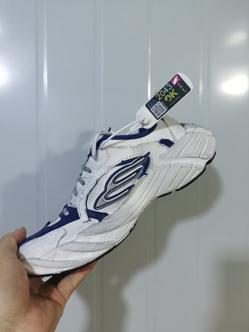 Navy and white low-top sneaker shown from the outer side, with layered panels, a contrasting side emblem, and a textured sole.