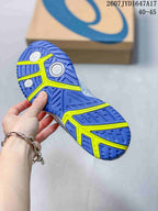 Close-up of the blue outsole with neon yellow sections and circular pivot details; an ASICS shoe box is visible in the background.