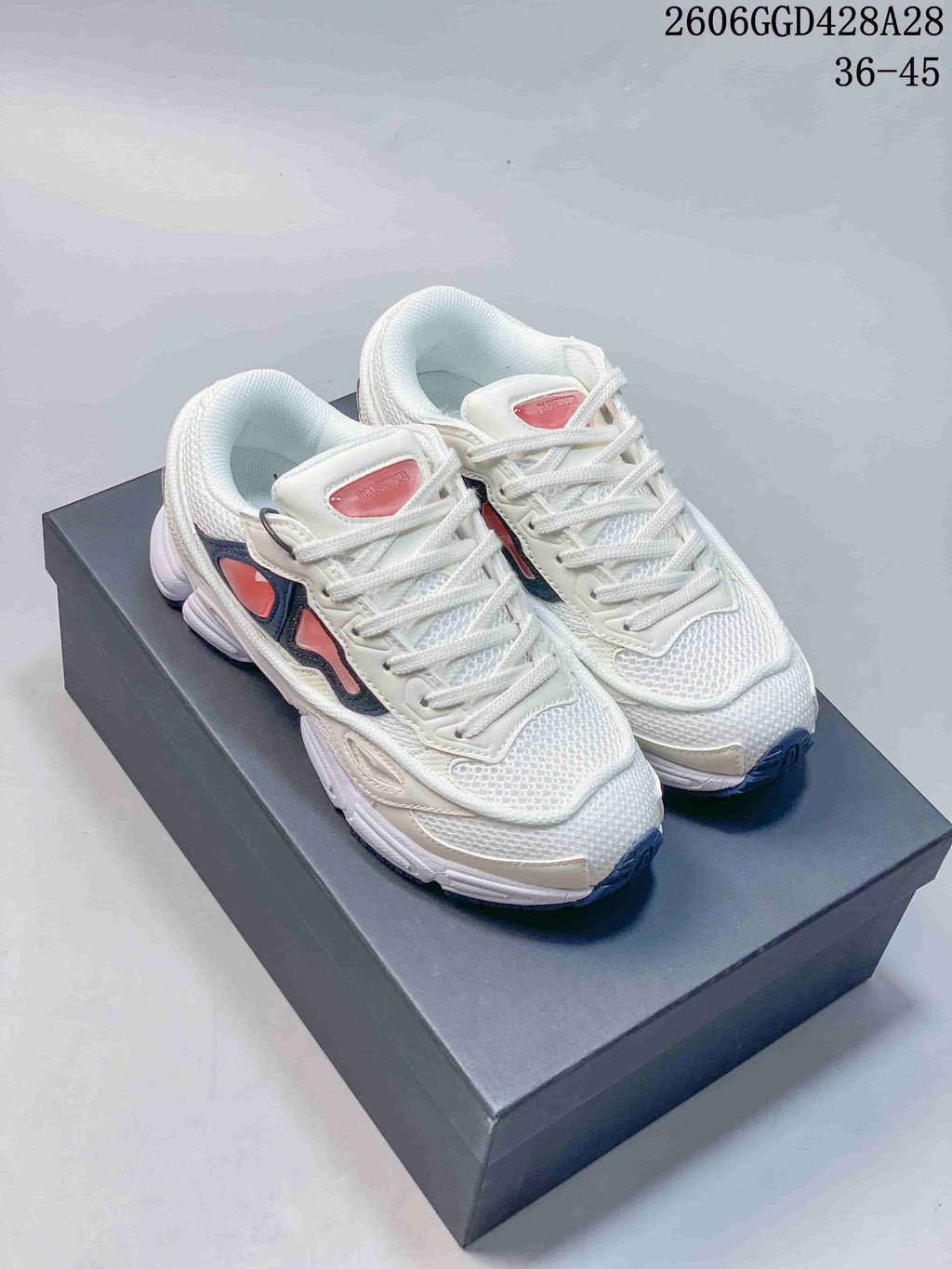 Pair of white Raf Simons Cylon-21 low-top sneakers with navy and coral-pink accents on a box