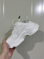 Side view of a white Balenciaga chunky sneaker showing layered panels, mesh inserts, round laces, and a sculpted sole.