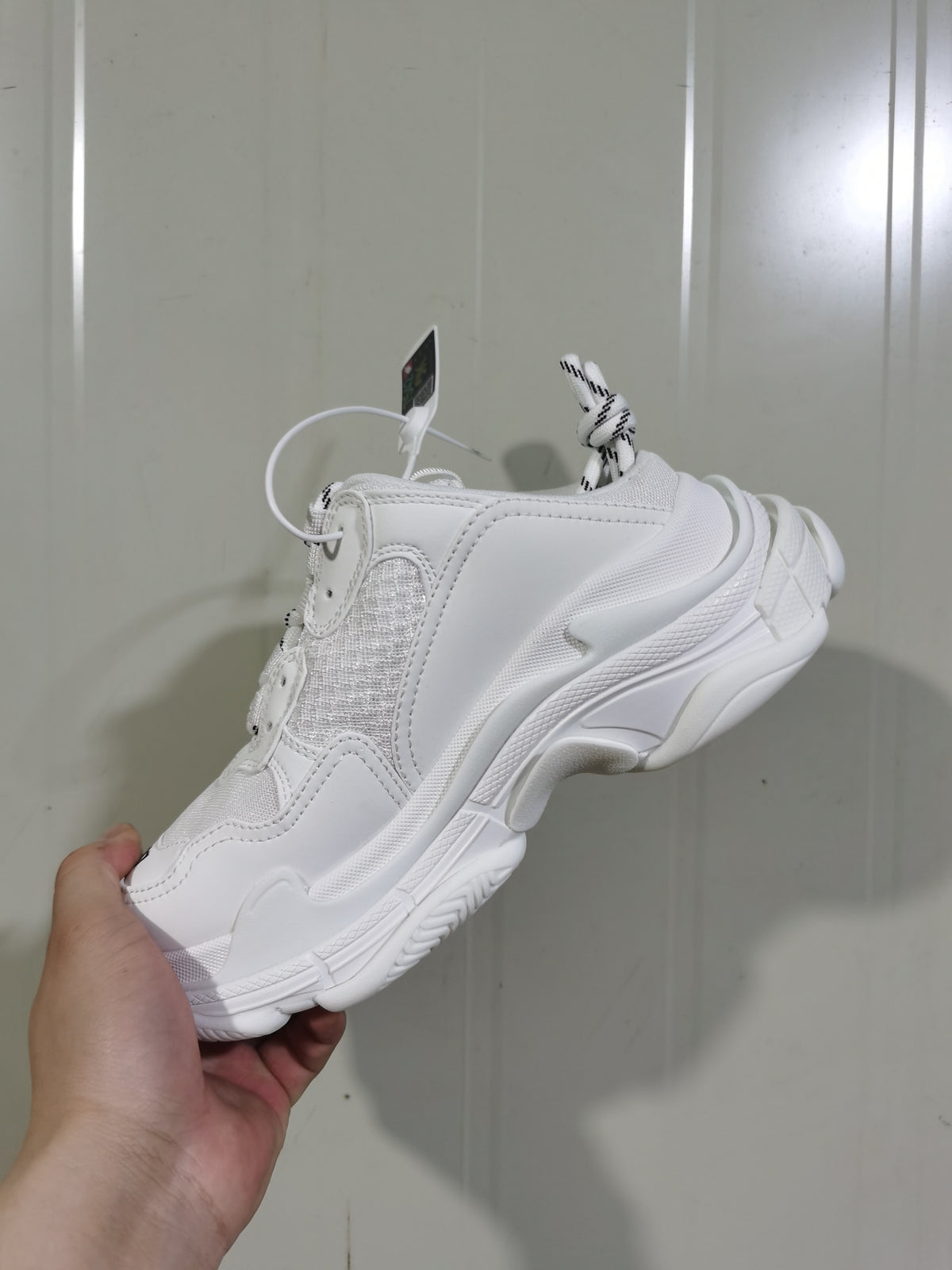 Side view of a white Balenciaga chunky sneaker showing layered panels, mesh inserts, round laces, and a sculpted sole.