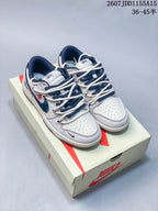 Pair of gray, white, and navy Nike SB Dunk Low sneakers displayed on a Nike shoebox; overlay shows style code 2607JDD1155A15 and size range 36–45.