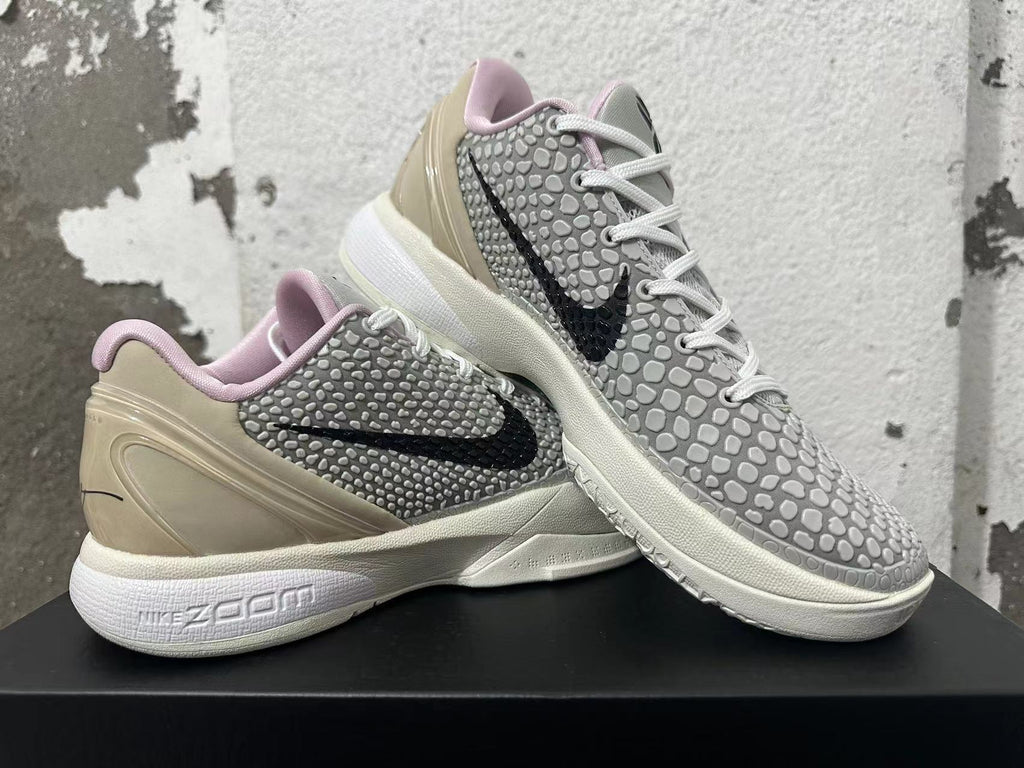 Pair of white and grey Nike basketball shoes displayed at an angle, showing black Swooshes and pale pink collar lining.