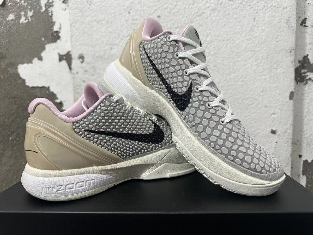 Pair of white and grey Nike basketball shoes displayed at an angle, showing black Swooshes and pale pink collar lining.