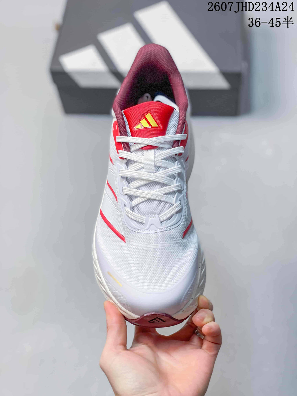 Top view showing the white laces, mesh-like white upper, red tongue and adidas logo detail.