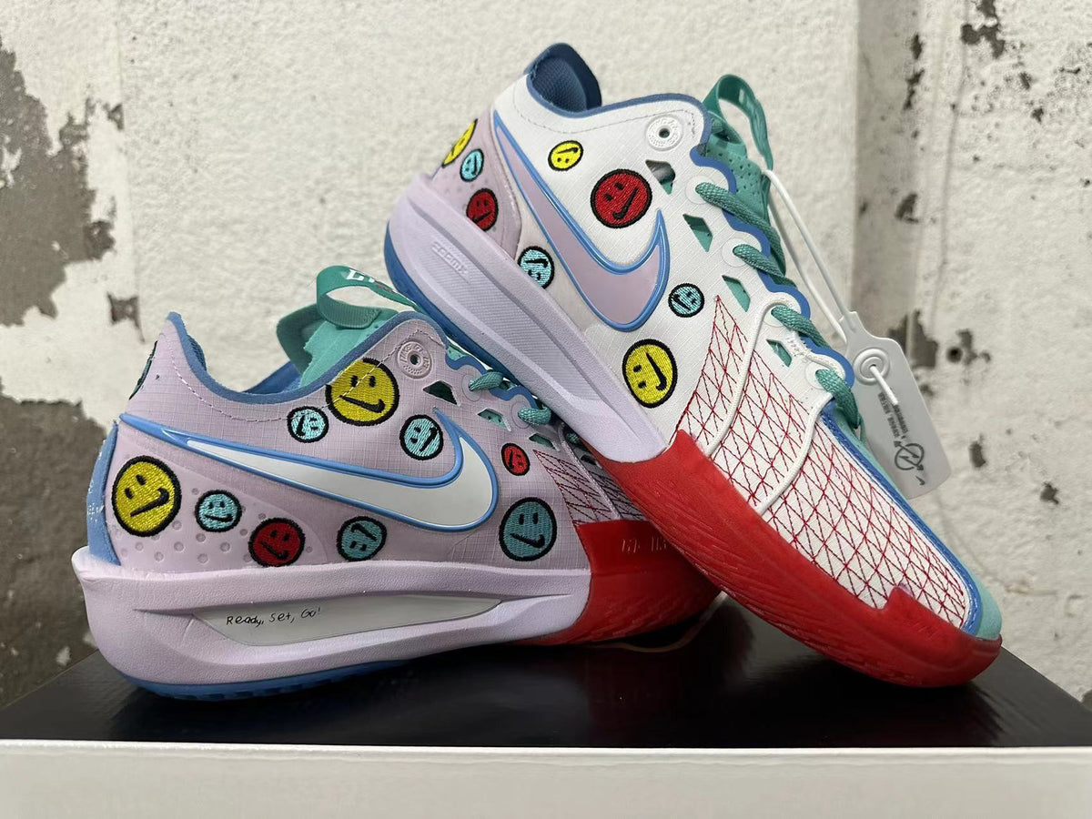 Pair of multicolor Nike basketball shoes with smiley graphics, turquoise laces, and red outsole accents.