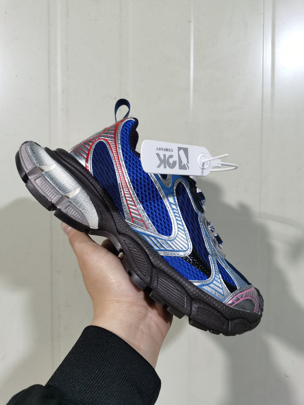Angled view of the royal blue and silver sneaker showing layered side overlays, mesh-style panels, pull tabs, and a segmented outsole.