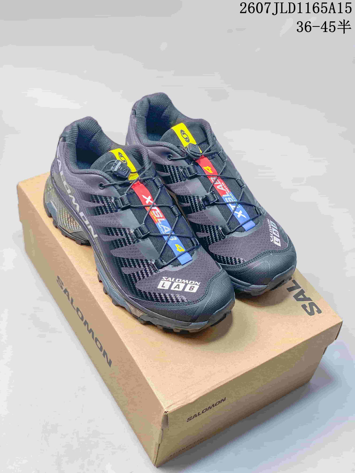 Pair of black Salomon XT-4 OG sneakers displayed on a Salomon shoebox, showing the layered upper and multicolor lace details.