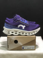 Side view of purple On Cloudmonster 3 shoes showing the blue heel panel, white sculpted midsole, and box.