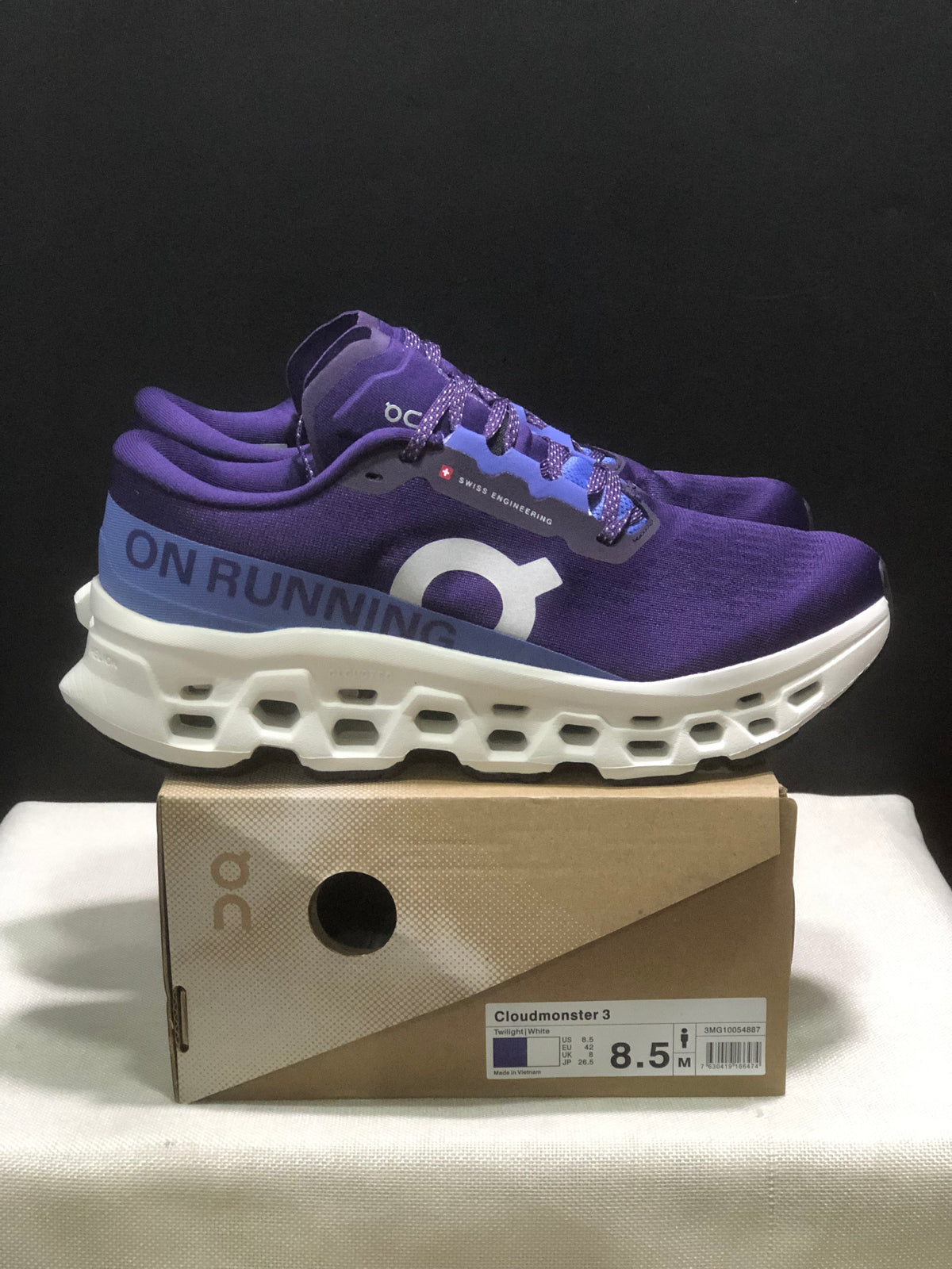 Side view of purple On Cloudmonster 3 shoes showing the blue heel panel, white sculpted midsole, and box.