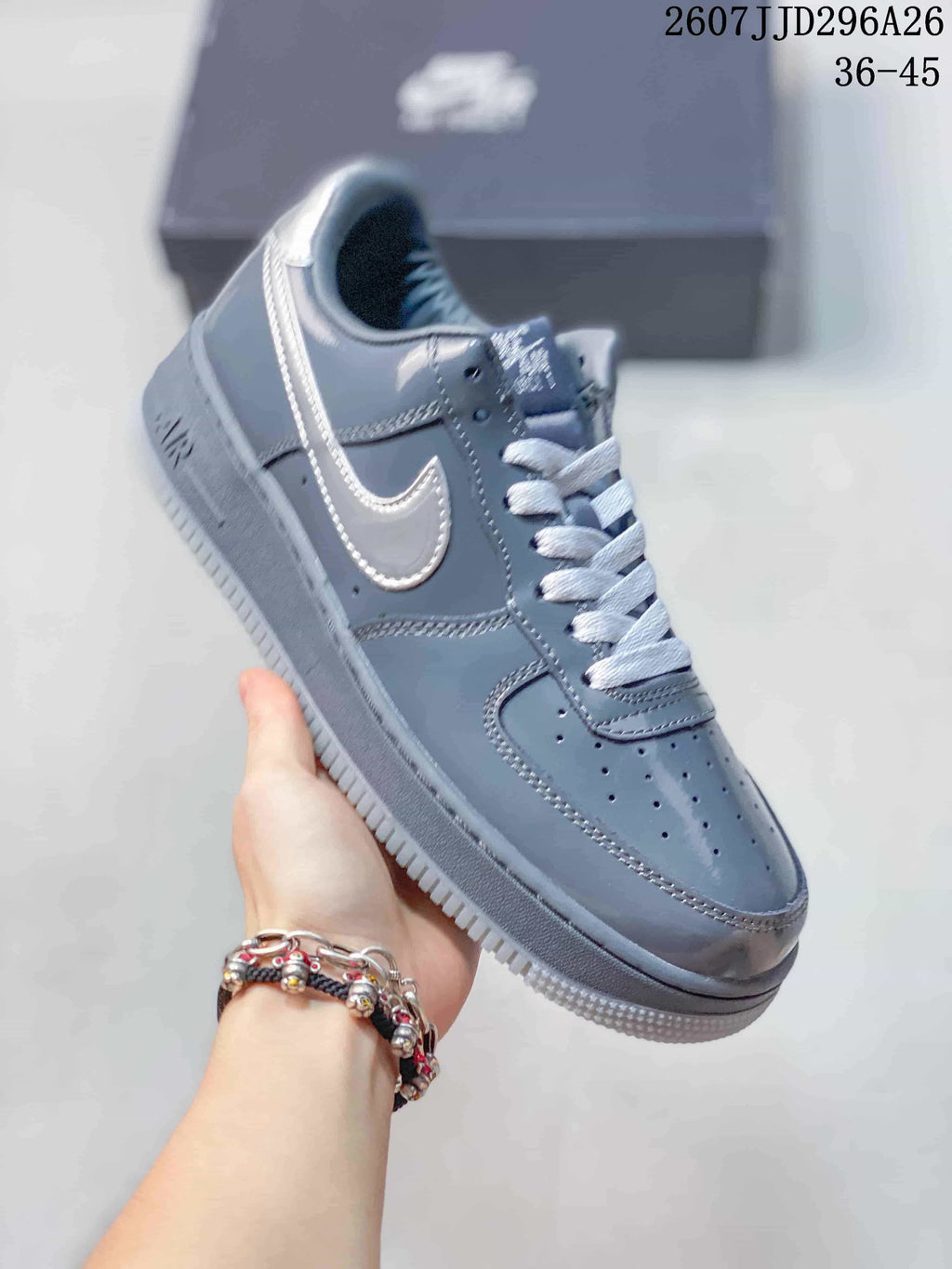 Angled side view of a grey Nike Air Force 1 sneaker with a contrasting Swoosh, white laces and textured outsole; image text shows 2607JJD296A26 and 36–45.