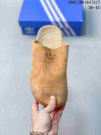 Top view of a tan closed-toe slip-on mule with a tonal Trefoil mark on the upper and a visible contoured footbed.