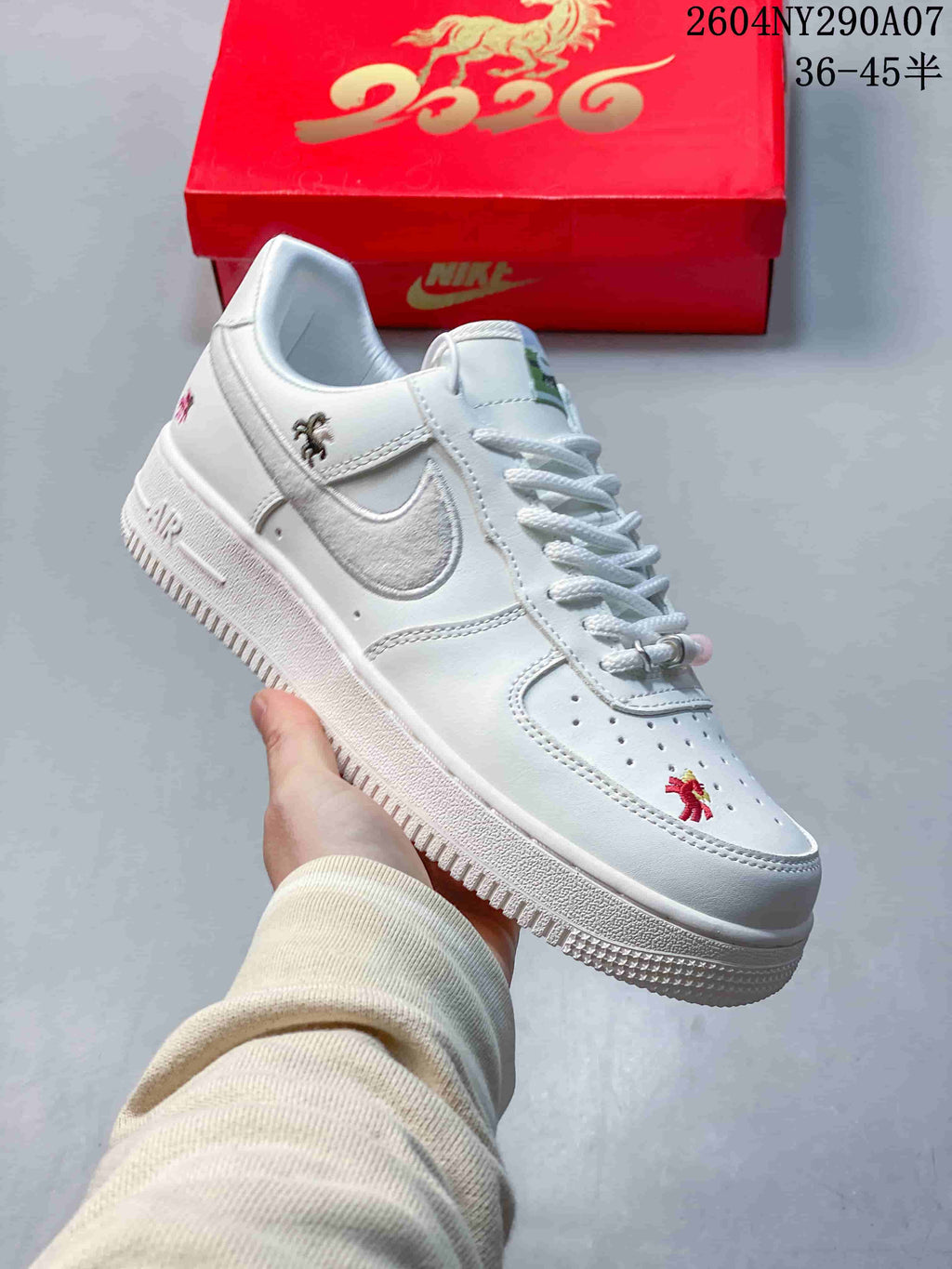 Angled side view of a white low-top sneaker with silver side detailing, embroidered accents, and a textured outsole.