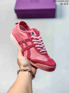 Red and pink Onitsuka Tiger sneaker held in hand, showing contrast stripes, white laces and a textured outsole.