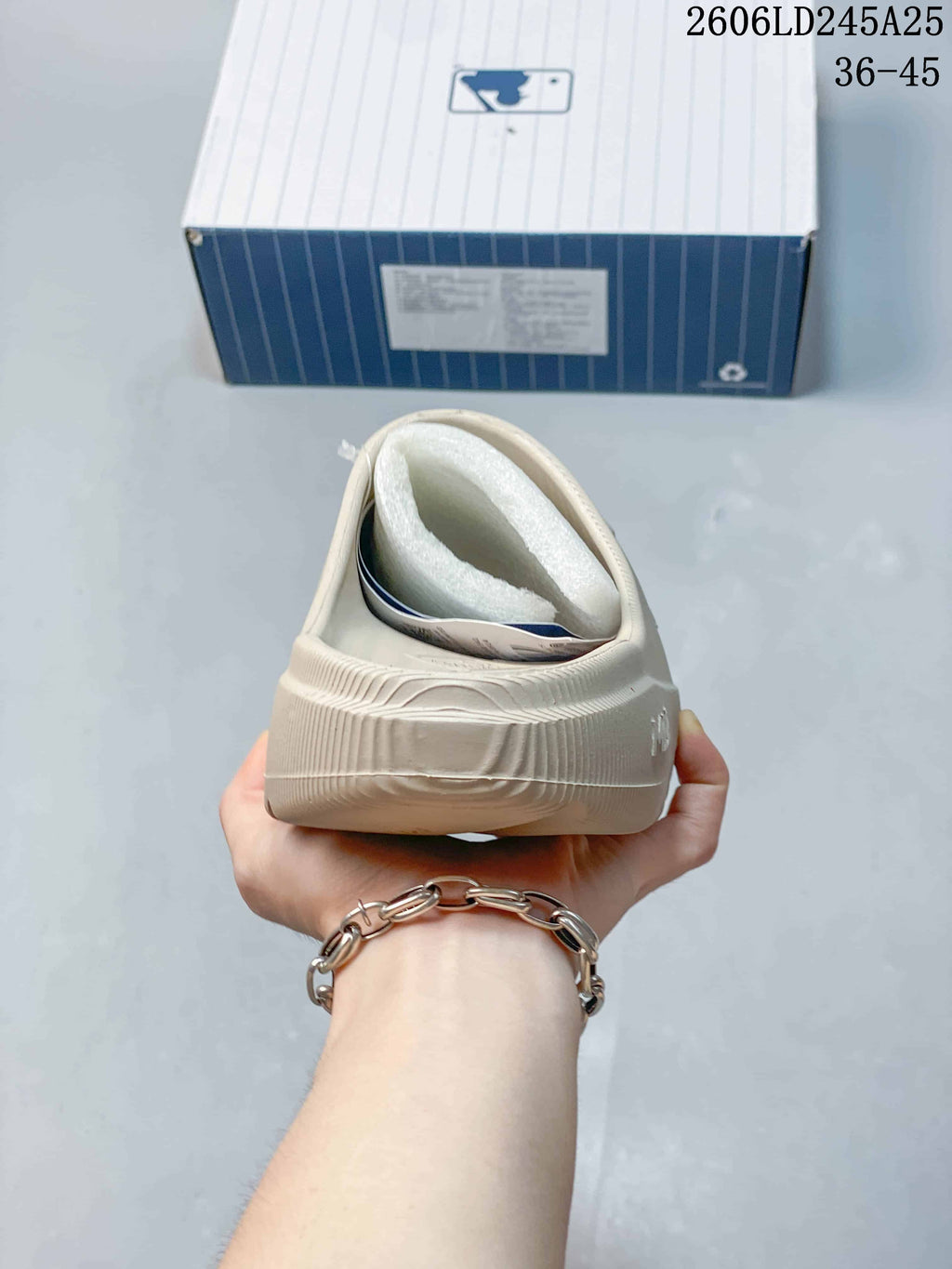 Rear view of a beige slide sandal showing the heel structure, textured upper, and shoe box in the background.