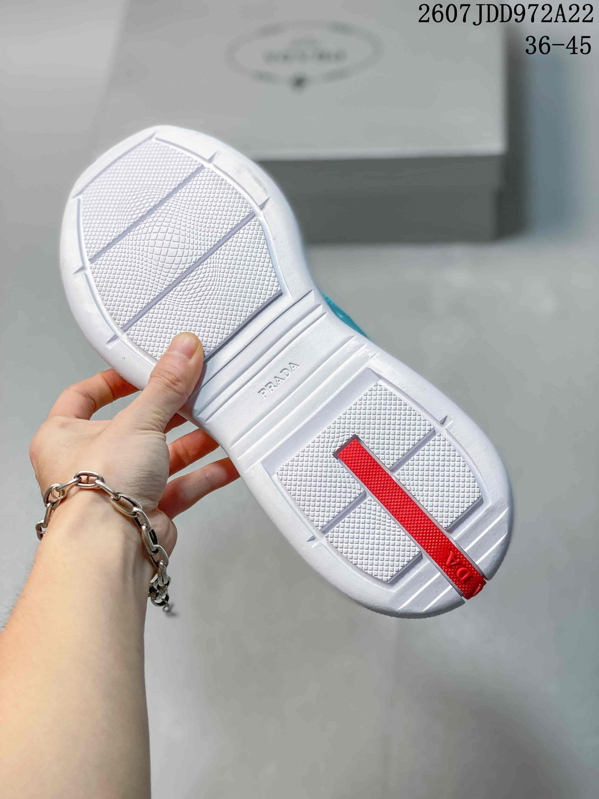Underside of the sneaker showing a white textured outsole, red heel detail, and Prada branding.