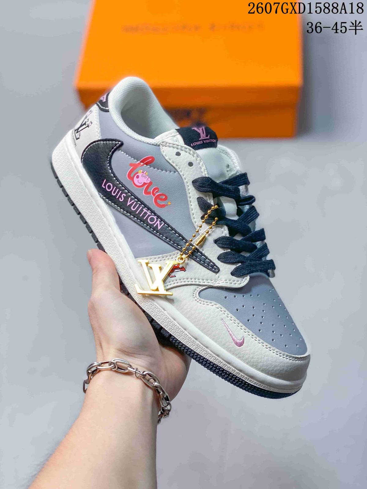 Angled side view showing the white and light gray low-top sneaker, dark navy side logo and outsole, decorative side graphics, and a gold-tone hanging accessory.