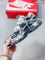 Side view of a Nike V5 RNR sneaker showing the layered silver and white upper, dark mesh panels and extended laces.