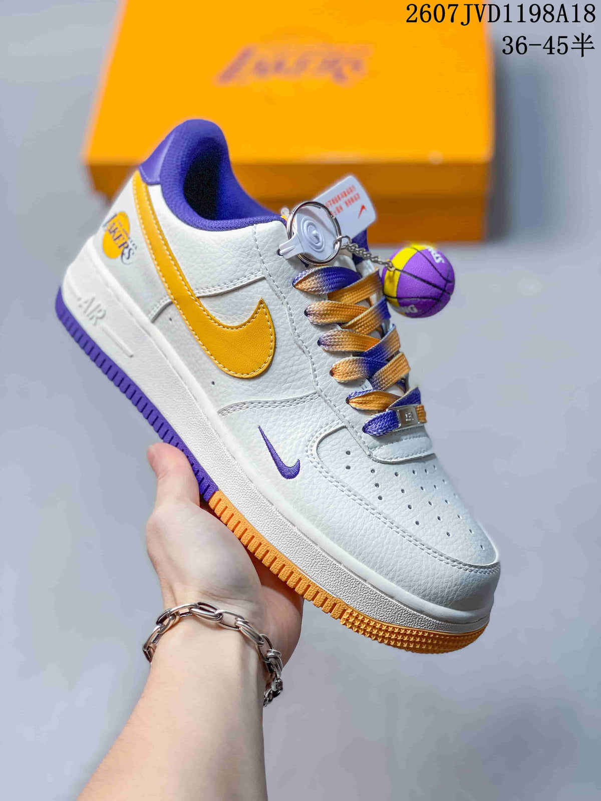 Close side view of a white sneaker with yellow and purple details, coordinating laces, and a basketball-shaped accessory.