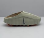 Side profile of a beige Nike open-back slip-on sandal with a dark Swoosh and orange outsole elements.