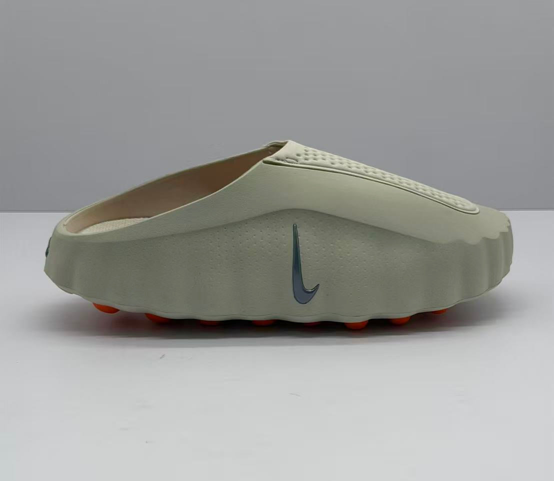 Side profile of a beige Nike open-back slip-on sandal with a dark Swoosh and orange outsole elements.