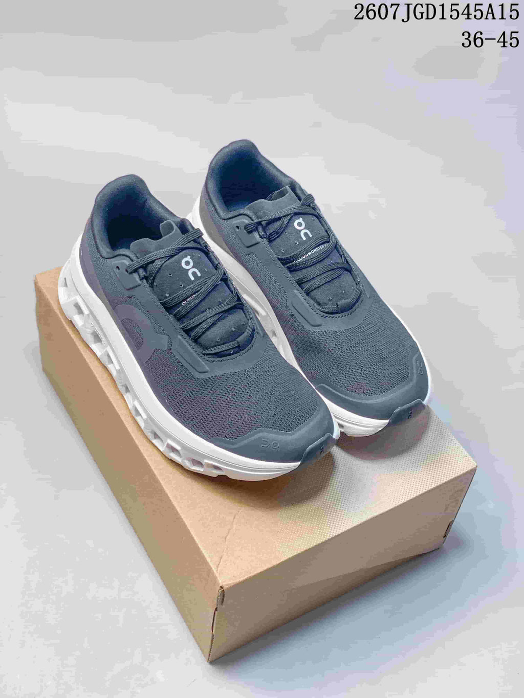 Pair of dark gray and white On CloudTilt sneakers displayed on a cardboard box; image text shows style code 2607JGD1545A15 and sizes 36–45.