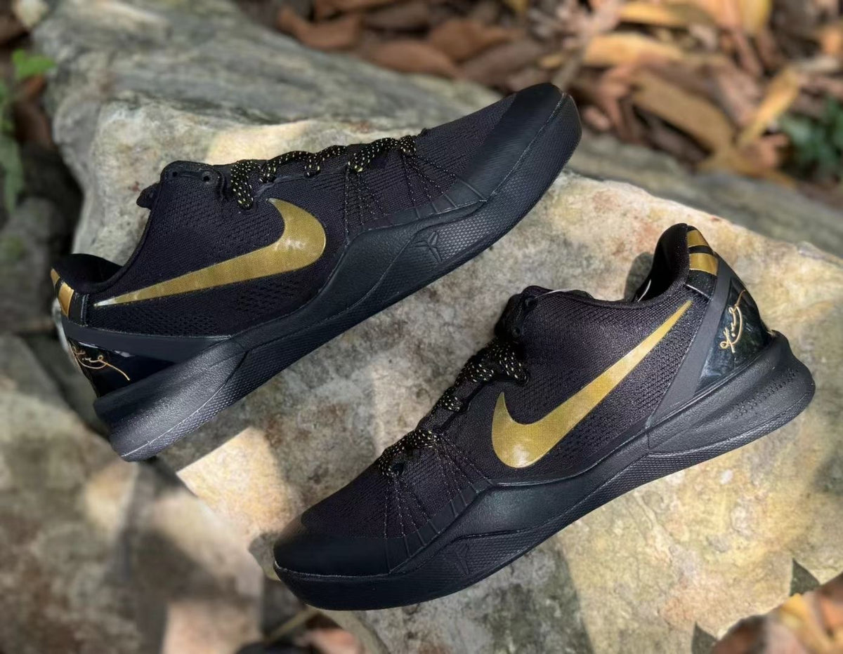 Pair of black and gold Nike Kobe 8 sneakers shown from an angled side view on rocks.