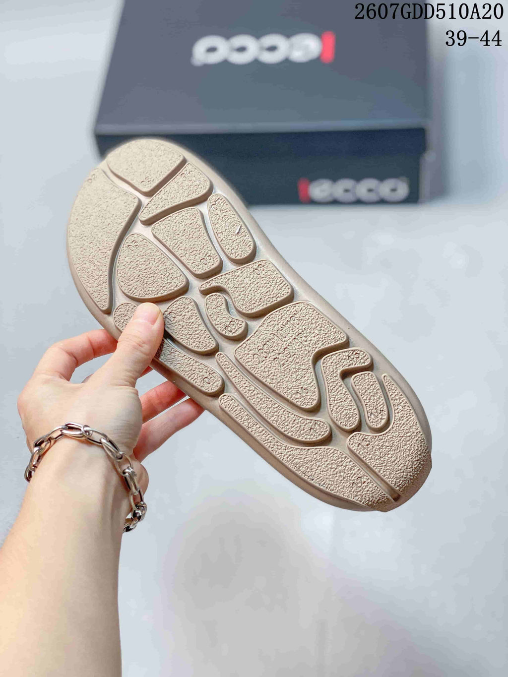 Close-up of the textured segmented outsole on a navy and tan ECCO sneaker; the background box shows the ECCO logo.