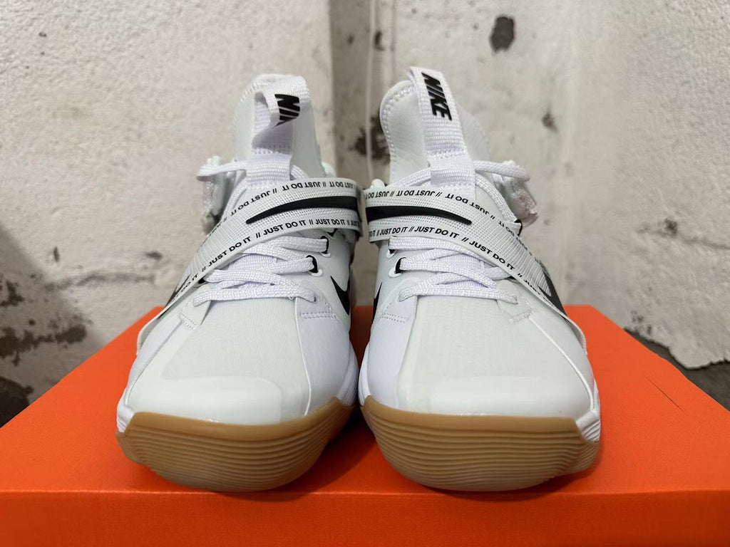 Front view of white Nike basketball shoes with black Swoosh details, printed straps, and gum-colored soles.