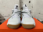 Front view of white Nike basketball shoes with black Swoosh details, printed straps, and gum-colored soles.