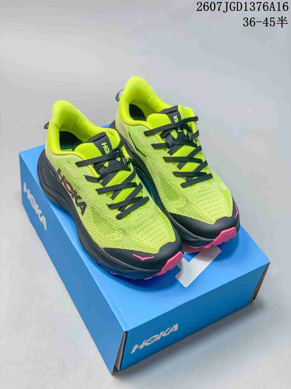 Pair of bright green and black HOKA running shoes with pink accents displayed on a blue shoe box.