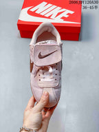 Front view of a pale pink Nike Classic Cortez sneaker showing its laces and fold-over tongue flap