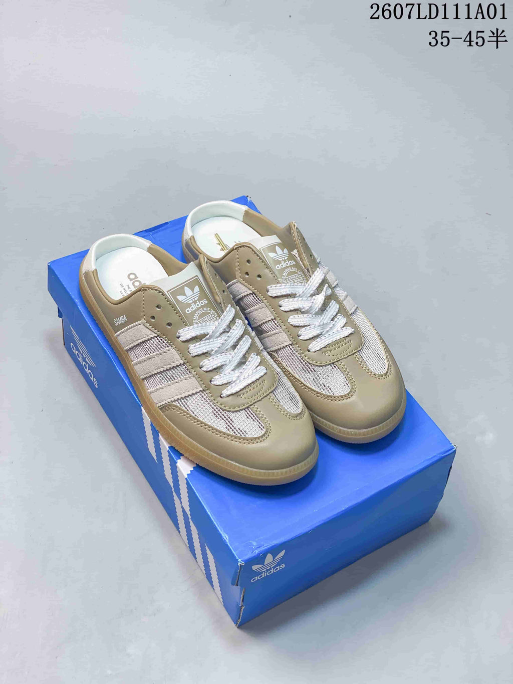 Pair of taupe and cream Adidas Samba low-top sneakers displayed on a blue shoe box