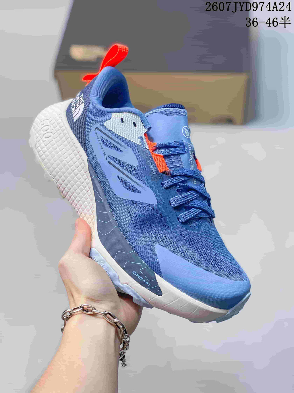 Angled side view showing the blue sneaker, orange heel pull tab, white midsole, and outsole tread.