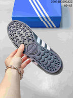 Bottom view of an adidas Samoa sneaker showing the patterned rubber outsole and blue shoebox.