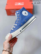 Side view of the blue high-top sneaker showing the circular ankle patch, metal eyelets, white stitching, and rubber sole.