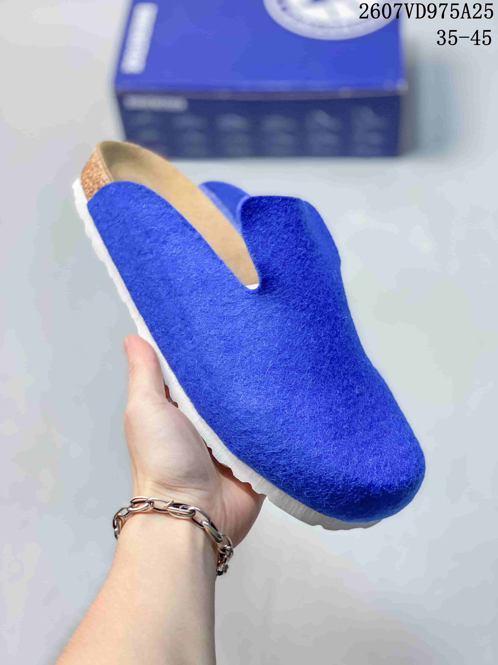 Angled close view of a blue closed-toe slip-on clog with a tan footbed area and white outsole.